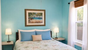 A bedroom with a bed, two bedside lamps, a ceiling fan, a framed picture on the wall, and a window with curtains.