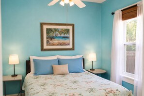 A bedroom with a bed, two bedside lamps, a ceiling fan, a framed picture on the wall, and a window with curtains.