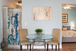 A room with a glass table, two chairs, a painting, a bed with a star pillow, and a plant on the table. - Waterfront 1BR Retreat w/Shared Private Beach + Walk to Beach Blvd (Gulfport)