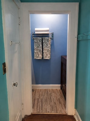 Ein Flur mit Holzboden, der zu einem Badezimmer mit blauer Wand und einem Handtuchhalter mit gemusterten Handtüchern führt.
