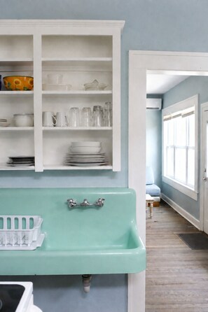 A bathroom with a mint green sink, white cabinets, and a window with blinds.