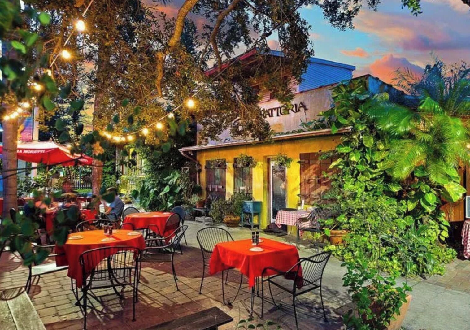 Un espace de restauration en plein air, avec des tables et des chaises, entouré de verdure et bordé par un bâtiment sur lequel on peut voir une enseigne.