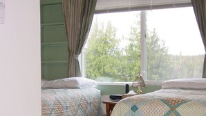 A bedroom with two beds, a window with curtains, a wooden floor, and a rug.