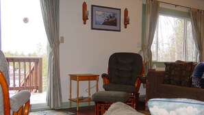 A living room with a wooden chair, a small table, a couch, and a window with curtains.