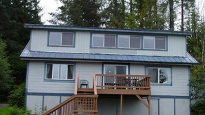 A two-story house with a wooden deck and a small staircase leading to a balcony.