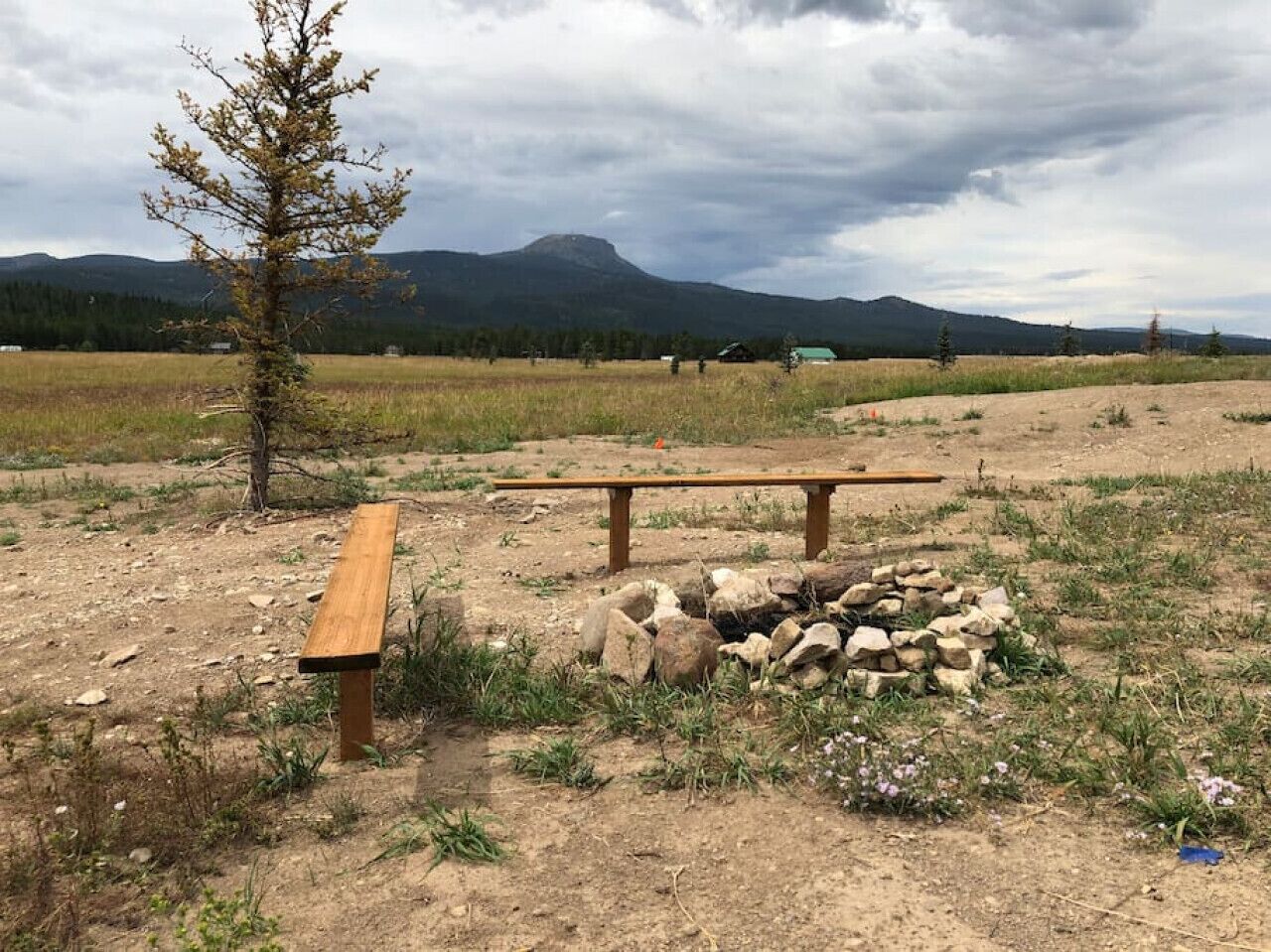 Un espace de pique-nique aménagé avec des bancs et un foyer, situé dans un cadre naturel avec des montagnes en arrière-plan.