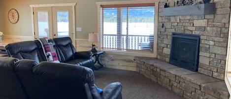 A living room with a stone fireplace, leather recliners, and a view through large windows.