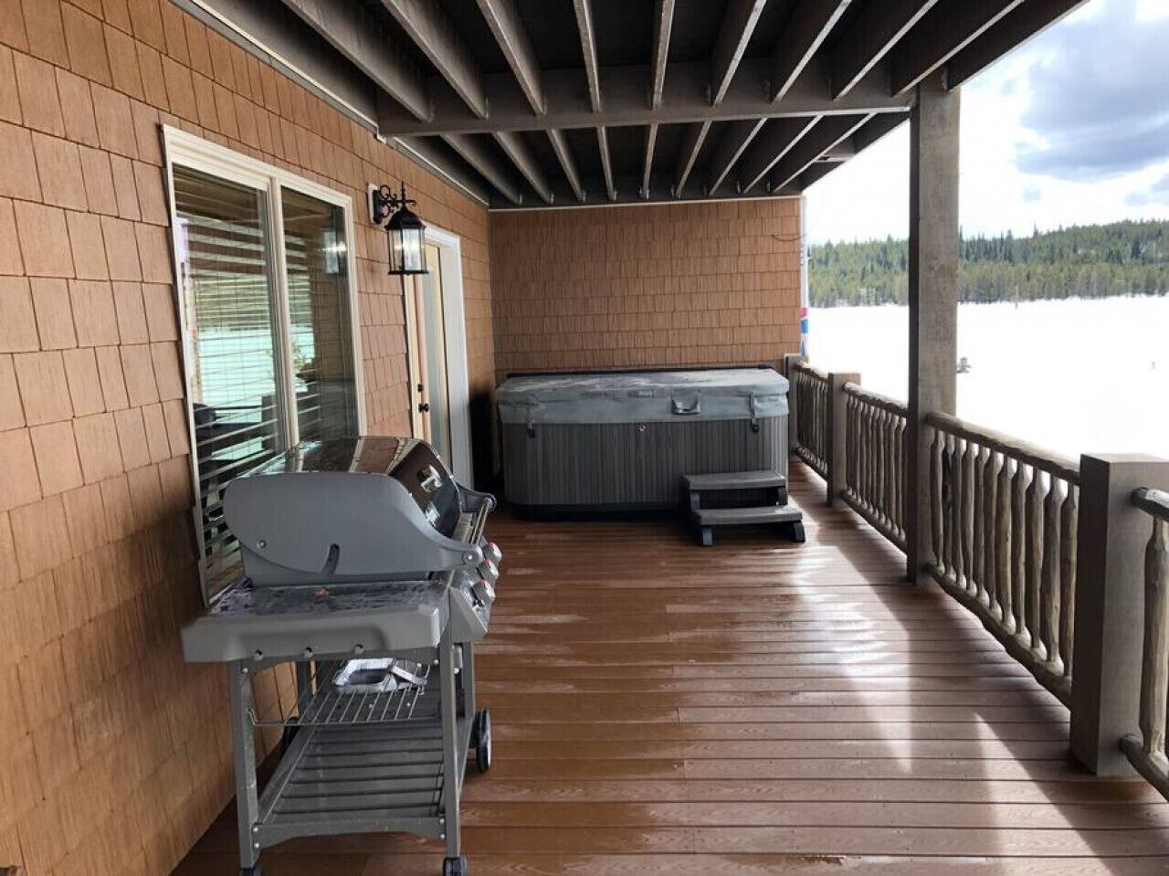 Eine überdachte Terrasse mit Grill und Whirlpool, mit Blick auf ein Gewässer.