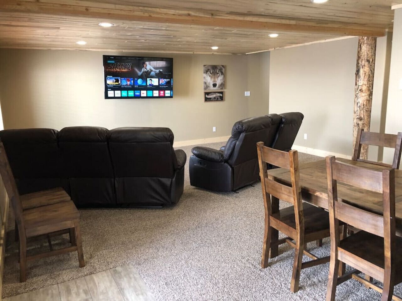 A living room with a black leather sofa, a recliner, and a wooden dining table with chairs.