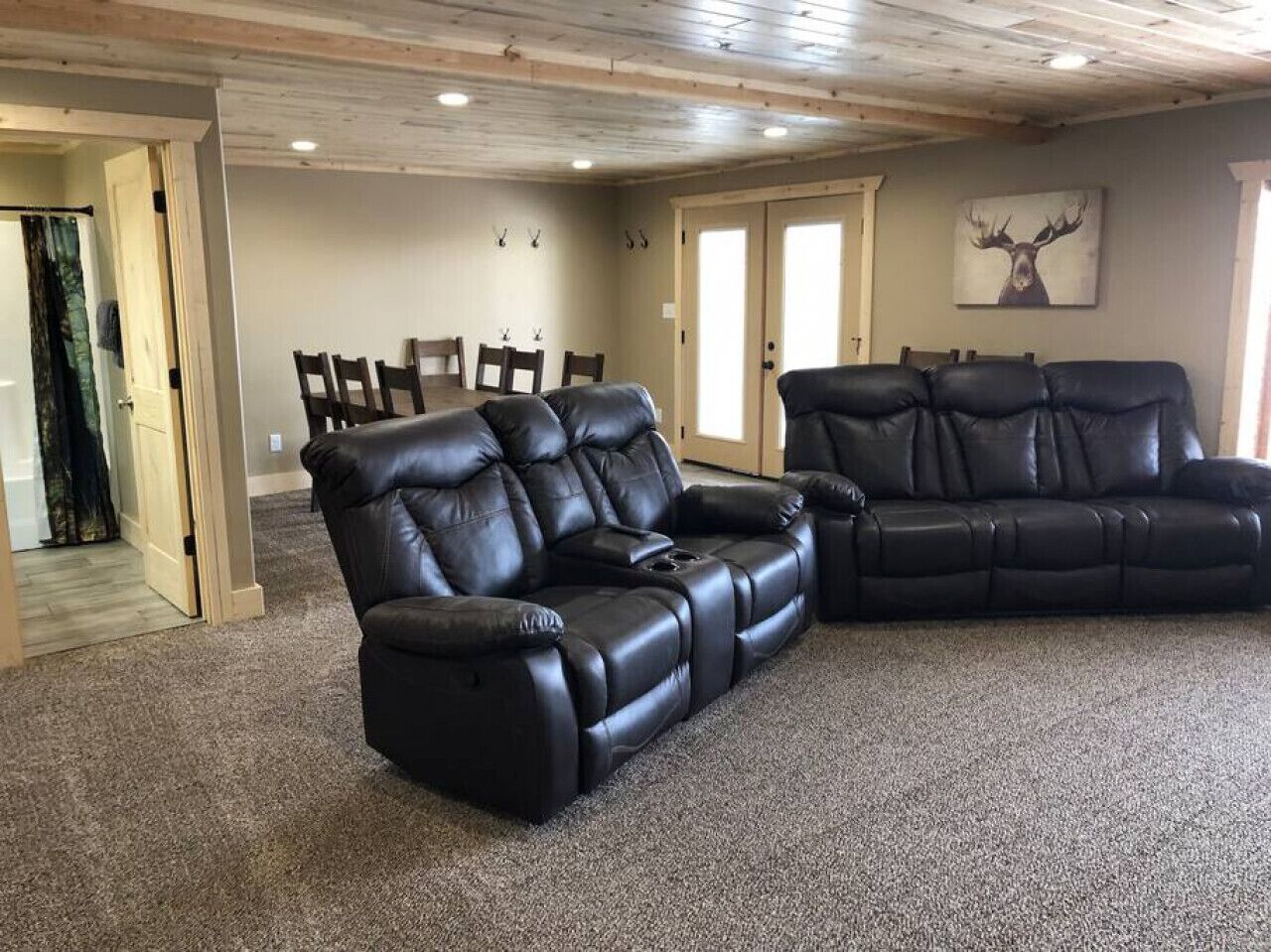 Un salon spacieux avec deux canapés en cuir noir et un grand tableau représentant un cerf accroché au mur.
