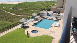 Área da piscina com espreguiçadeiras e guarda-sóis, uma banheira de hidromassagem e vista para a praia e oceano.