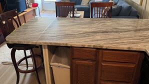A kitchen with a marble countertop, wooden cabinets, and a dining area with chairs and a table.