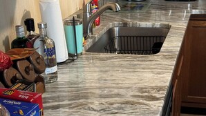 A kitchen with a marble countertop, a sink, a coffee maker, and various food items.