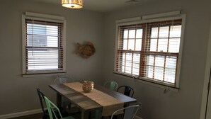A dining area with a wooden table, four chairs, and two windows with blinds.
