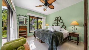 Une chambre d’hôtel avec un lit, deux lampes de chevet, un ventilateur de plafond, une fenêtre avec des rideaux et une vue sur la verdure.