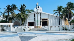 Eine weiße Kirche mit Statue auf dem Dach, Palmen und einem Kreuz am Gebäude.