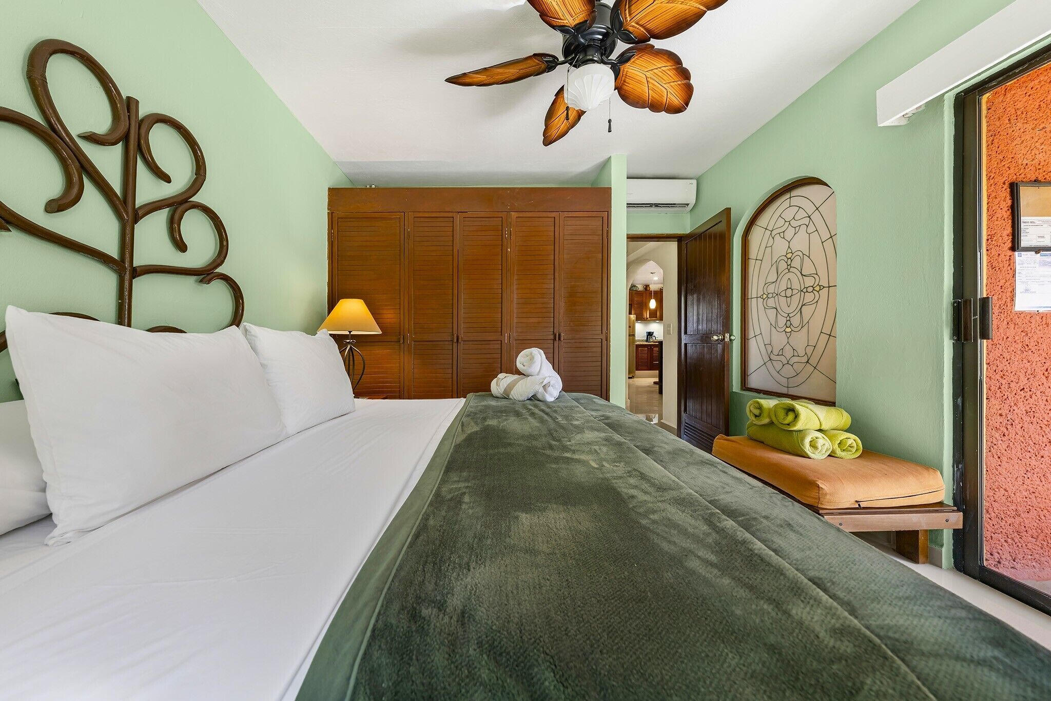 Habitación de hotel con cama, cabecero de madera, ventilador de techo, armario de madera y ventana con vistas al exterior.