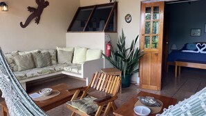 A cozy living room with a sofa, a wooden chair, a hammock, a dining table, and a door leading to a bedroom. - Gorgeous Views of Pacific and Rainforest (manuel antonio)