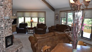 A living room with a fireplace, leather sofas, a ceiling fan, and large windows with blinds. - Waterfront Lake House on Scenic Lake Nokomis (Tomahawk)