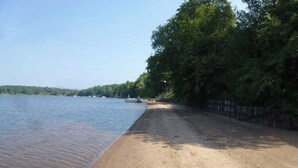 A sandy beach with a wooden fence and trees in the background. - Waterfront Lake House on Scenic Lake Nokomis (Tomahawk)