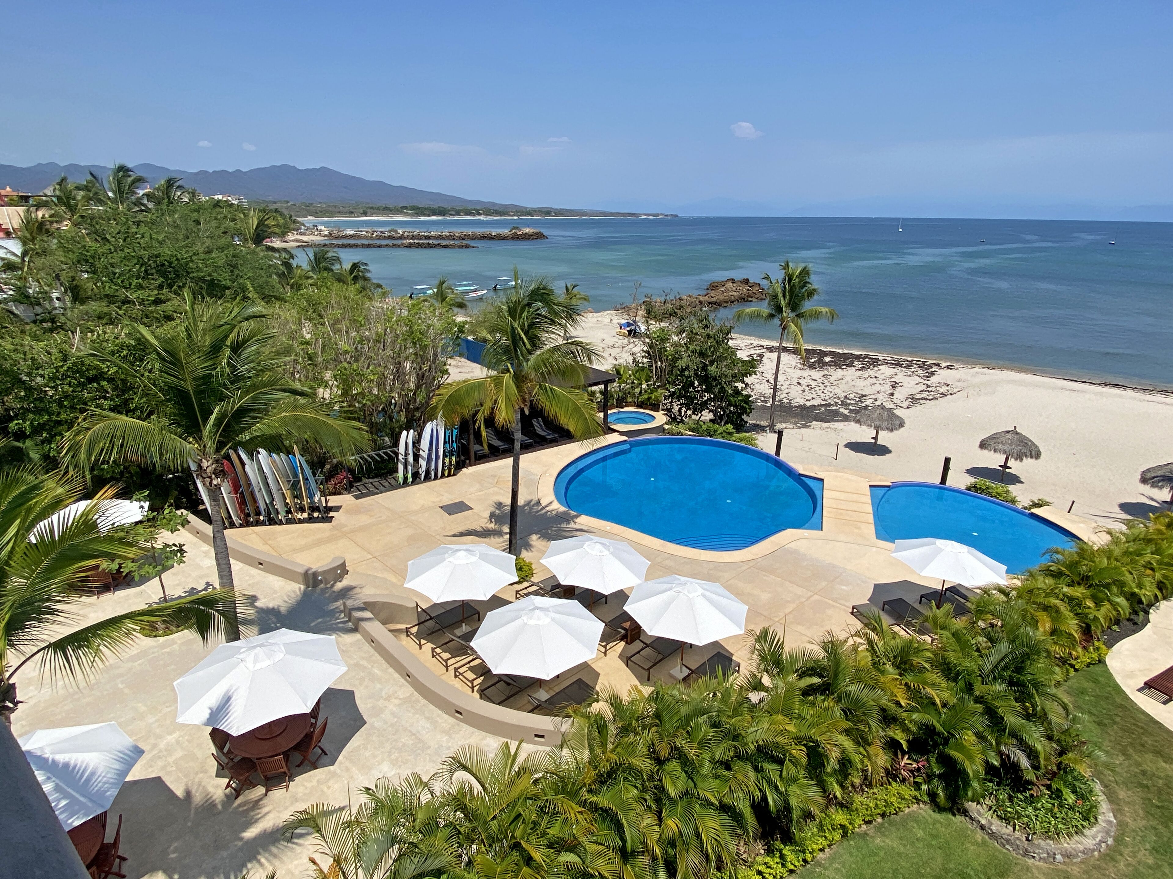 Un complexe hôtelier doté de deux piscines, de coins salon au bord de la plage et de palmiers.