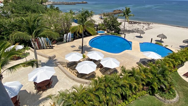 Ein Resort mit zwei Swimmingpools, Sitzgelegenheiten am Strand und Palmen.