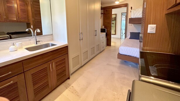 Een moderne keuken met een spoelbak, kasten en een aanrecht. Er is een bed met hoofdeinde en nachtkastje.