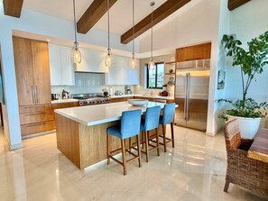 A modern kitchen with a central island, bar stools, stainless steel appliances, and wooden cabinetry. - FRONT ROW PENTHOUSE - Amazing views -  Premier/Cook/Golf Cart (Punta De Mita)
