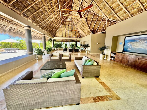 A spacious lobby with a thatched roof, comfortable seating areas, and a large TV screen displaying a map. - FRONT ROW PENTHOUSE - Amazing views -  Premier/Cook/Golf Cart (Punta De Mita)