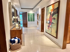 Un pasillo con piso pulido, un espejo, un jarrón decorativo con flores, una vela y una cesta con toallas.