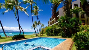 A swimming pool with a clear view of the ocean, surrounded by palm trees and a building with balconies. -  3 Bedroom, 3 Bath Oceanfront Condo With Amazing Views of Molakai and Lanai  (Lahaina)