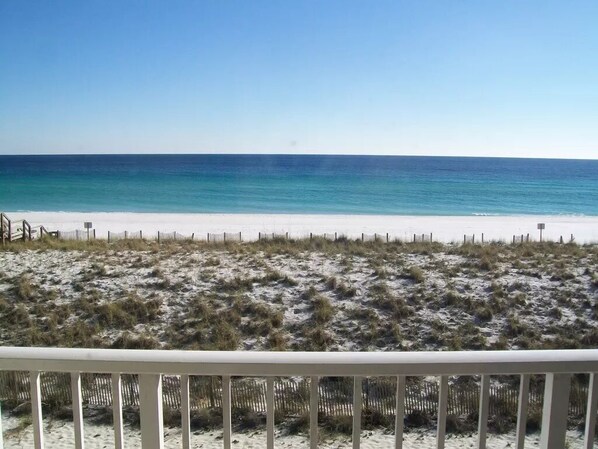 A beach with a white fence in the foreground and a clear view of the ocean.