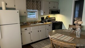 Una cocina con armarios blancos, un refrigerador, un microondas, una estufa y una mesa de comedor con manteles individuales.