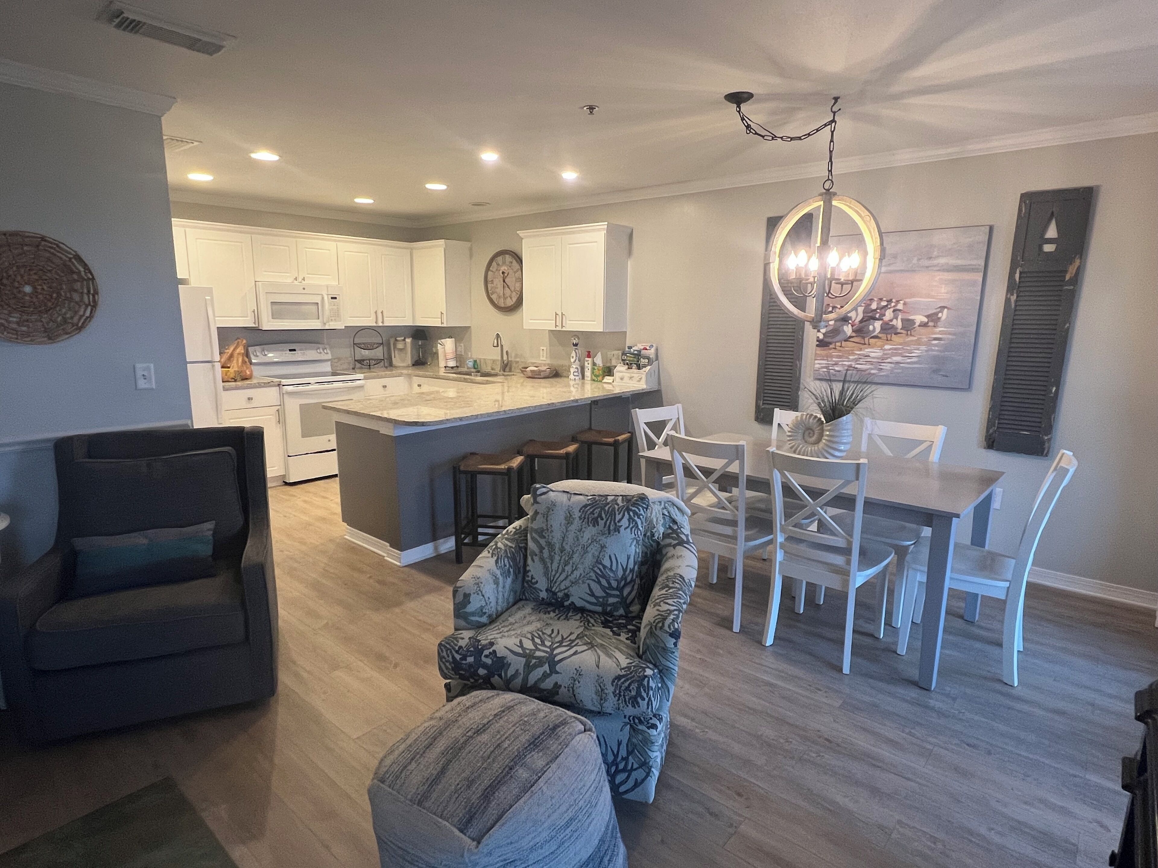 A modern kitchen with white cabinets, a central island, and a dining area with white chairs and a table.