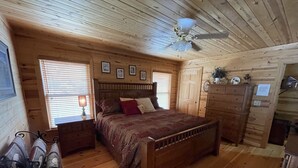 A wooden cabin bedroom with a bed, dresser, and ceiling fan.