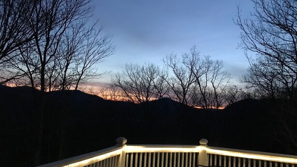 A deck with a railing, overlooking a mountainous landscape during twilight.