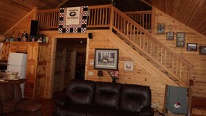 A cabin interior with a wooden staircase, a leather couch, and a ceiling fan.