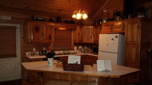 A wooden cabin interior with a kitchen area featuring wooden cabinets, a refrigerator, and a dining table with benches.