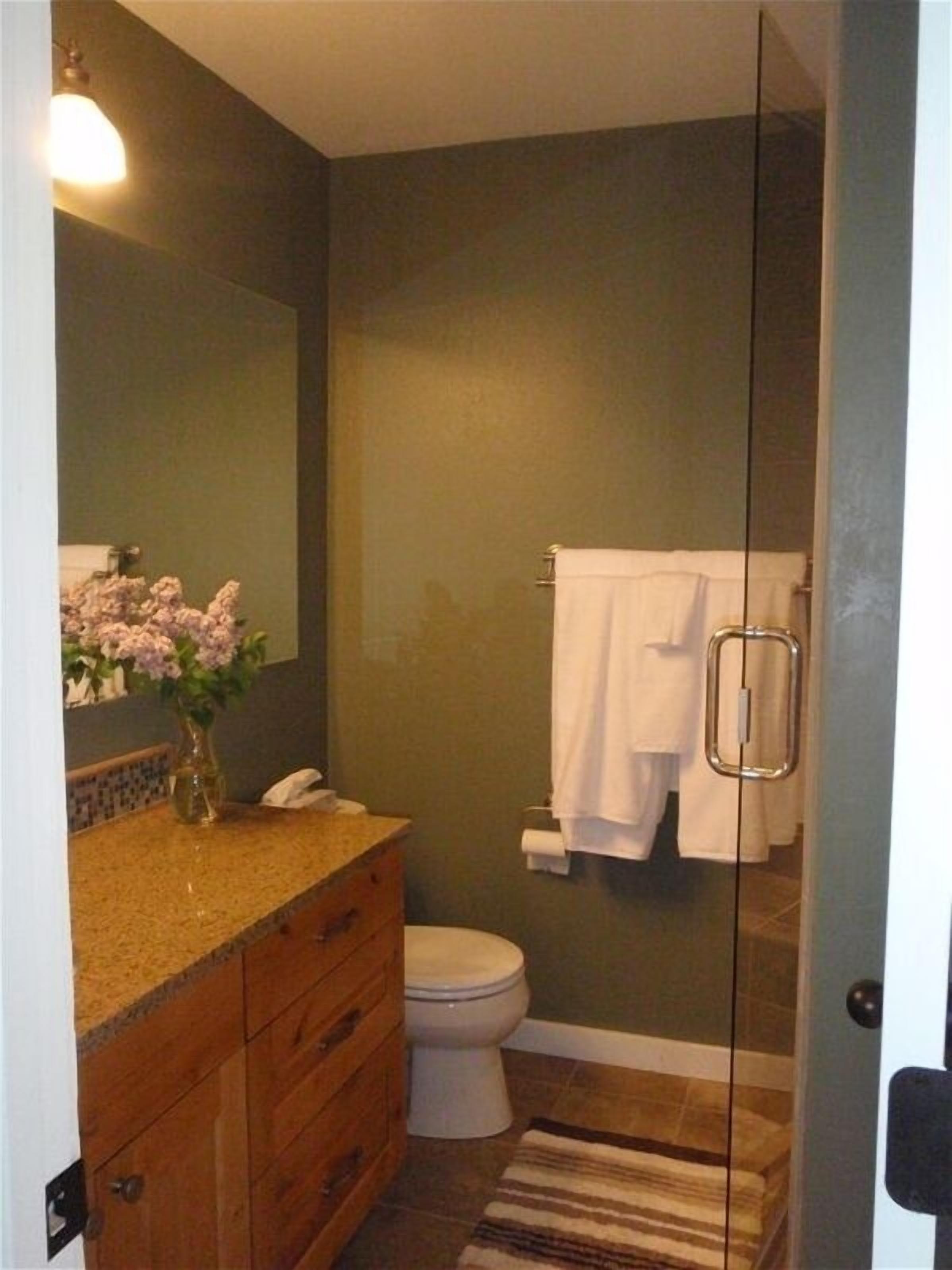 A bathroom with a wooden vanity, a toilet, a glass shower enclosure, and a mirror.