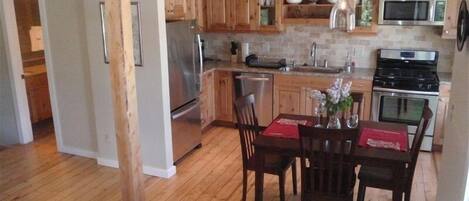 A kitchen with wooden cabinets, stainless steel appliances, and a dining area with a table and chairs.