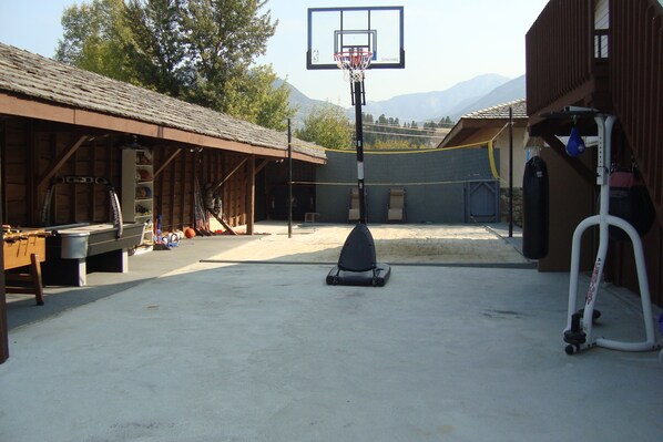 An outdoor basketball court with a net, a trampoline, and a covered seating area with tables and chairs.