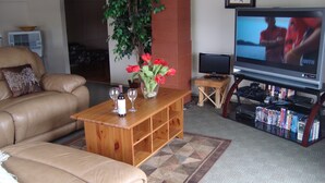 A living room with a leather sofa, a wooden coffee table with wine glasses, a TV, and a bookshelf. - ** Ypcfitness & Accomodations ** (Invermere)
