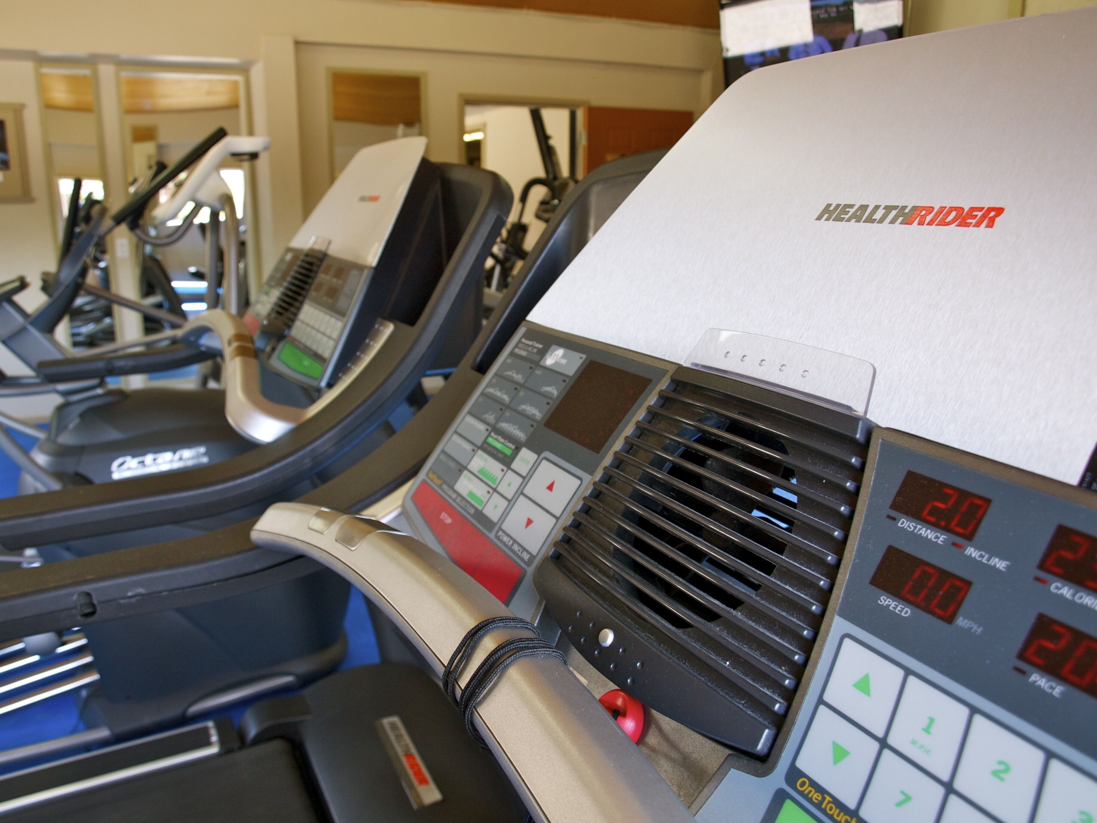 A treadmill with a digital display and control panel, indicating speed, distance, and incline.