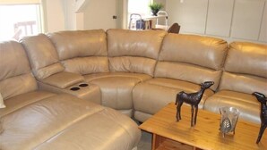 A tan leather sectional sofa with a wooden coffee table and decorative horse figurines. - ** Ypcfitness & Accomodations ** (Invermere)