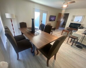 Uma sala de jantar com mesa e cadeiras de madeira, TV fixada na parede e ventilador de teto.