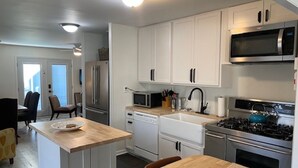 A modern kitchen with white cabinets, a microwave, a stove, and a dishwasher. There is a wooden dining table with chairs.