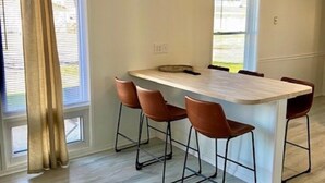 A modern kitchen with a central island, four bar stools, and large windows with curtains.