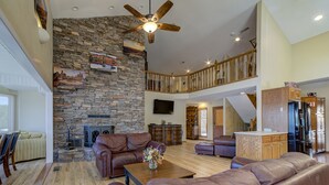 Ein geräumiges Wohnzimmer mit Steinwand, Ledersofas, einem Holztisch und einem Deckenventilator.