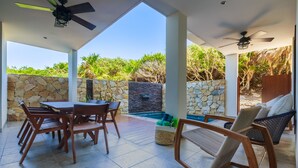 Eine überdachte Terrasse im Freien mit Steinwand, Pool, Holzmöbeln und Deckenventilatoren.