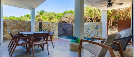 Un patio techado al aire libre con pared de piedra, piscina, muebles de madera y ventiladores de techo.